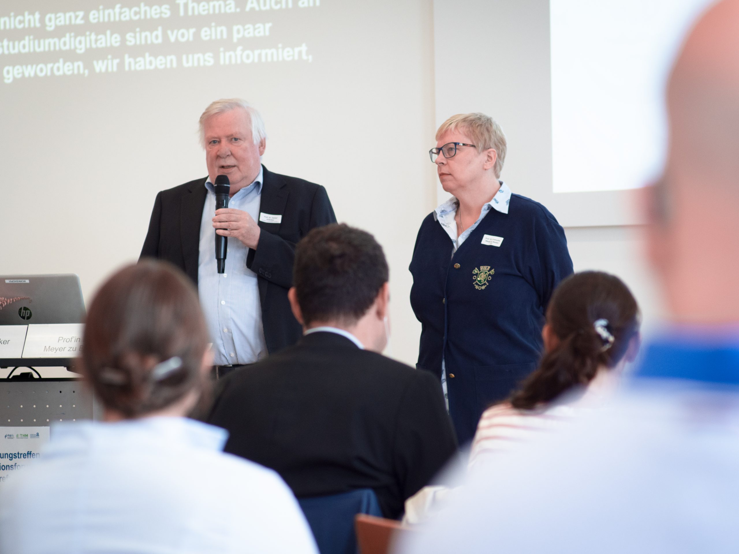 Prof. Dr. Krömker und Prof. Dr. Meyer zu Bexten sprechen vor dem Publikum.