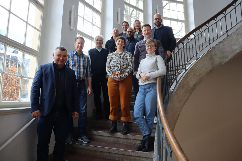 Von Links nach Rechts: Daniela Diekmann, Noreen Krause, Markus Deimann, Alexander Clauss, Martin Lentz, Sebastian Metag, Peter Rempis, Paulina Rinne, Tim Wiegers, Verena Ruslies und Konrad Faber im dynamischen Abgang von der Treppe im Gebäude der Bauhaus-Universität. 