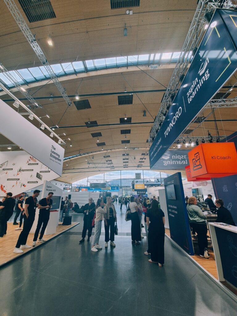 Ein Gang in einer großen Messhalle. Rechts uns links stehen Messestände.