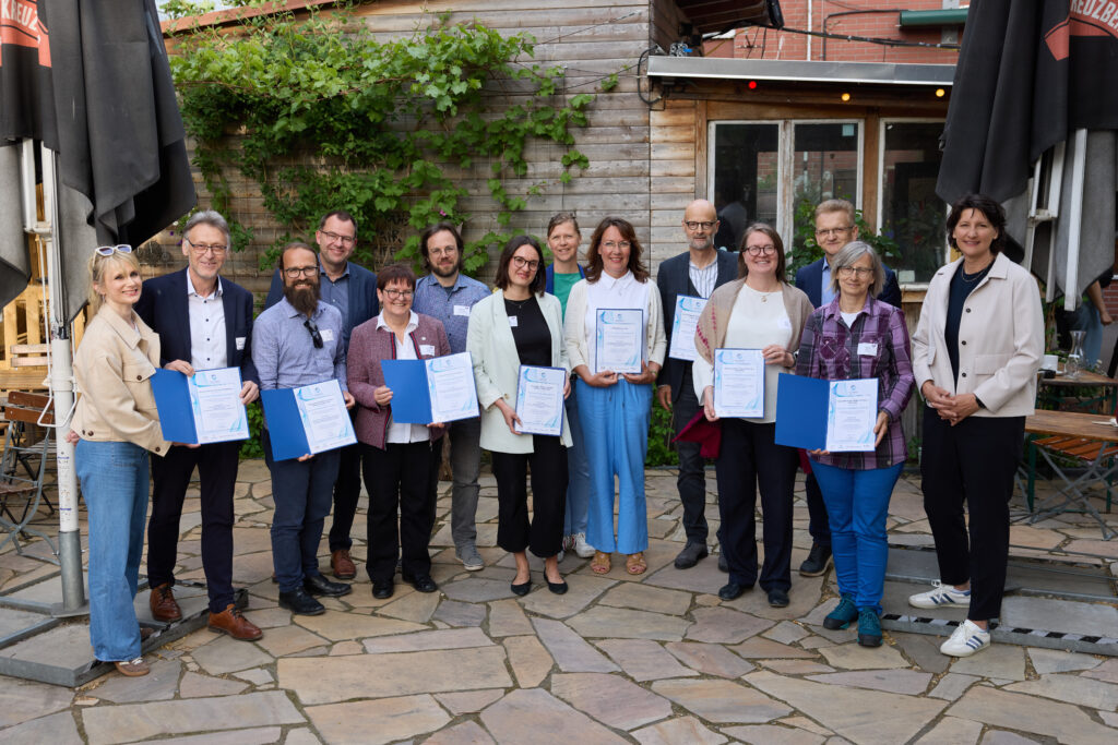 Die Teilnehmenden der Peer-to-Peer-Verbundberatungen des Hochschulforum Digitalisierung stehen zum Gruppenfoto zusammen. Sie halten alle ihre Zertifikate in der Hand.