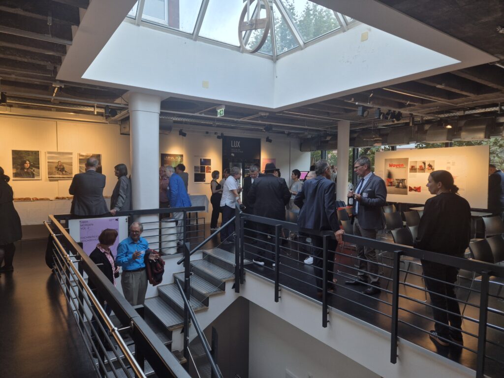 Foto: Einige Personen stehen in einem Foyer  an einem Treppenabgang und unterhalten sich.